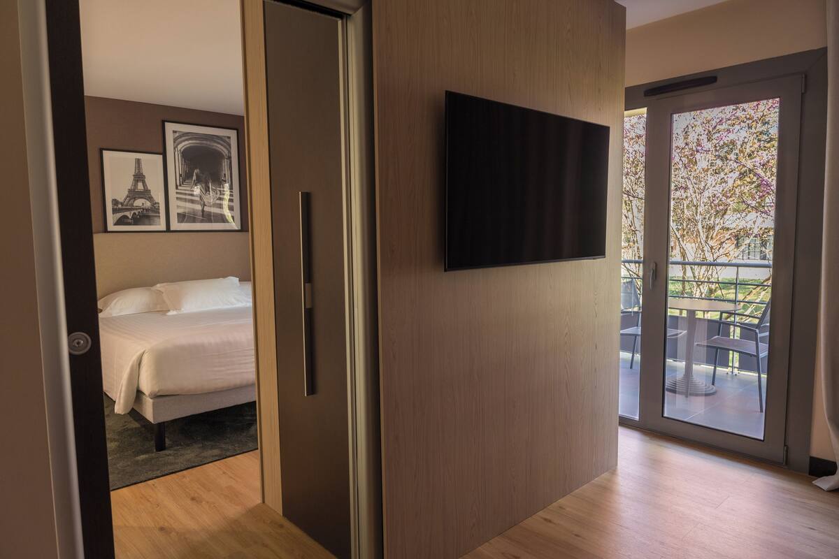 Een moderne hotelkamer met een bed, een flatscreen televisie en een balkon met tuinmeubilair.