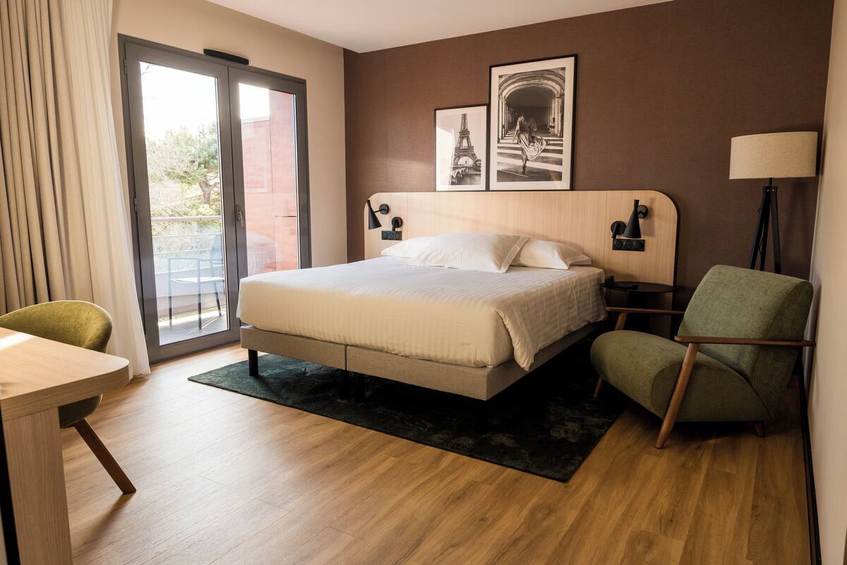 Een hotelkamer met een bed, een stoel, een tafel, een lamp en twee foto's in lijsten aan de muur.