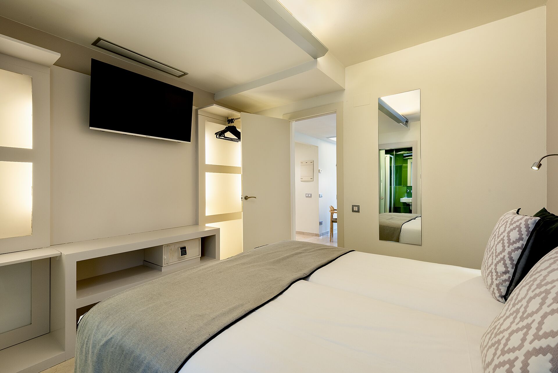 Une chambre à coucher moderne avec un lit, un téléviseur fixé au mur, un banc et un miroir.