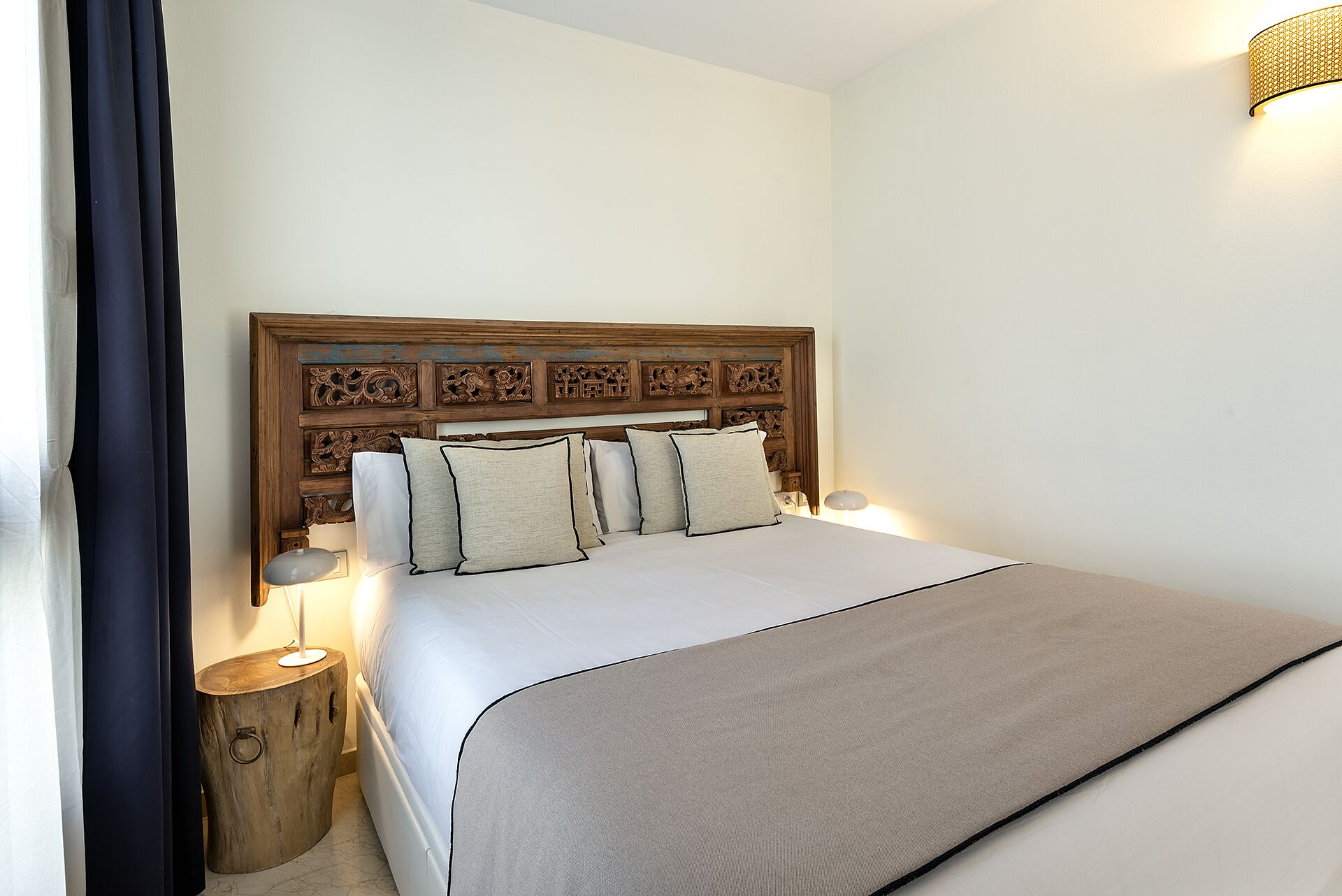 A neatly made bed with a wooden headboard, a bedside table, and a wall-mounted light fixture.