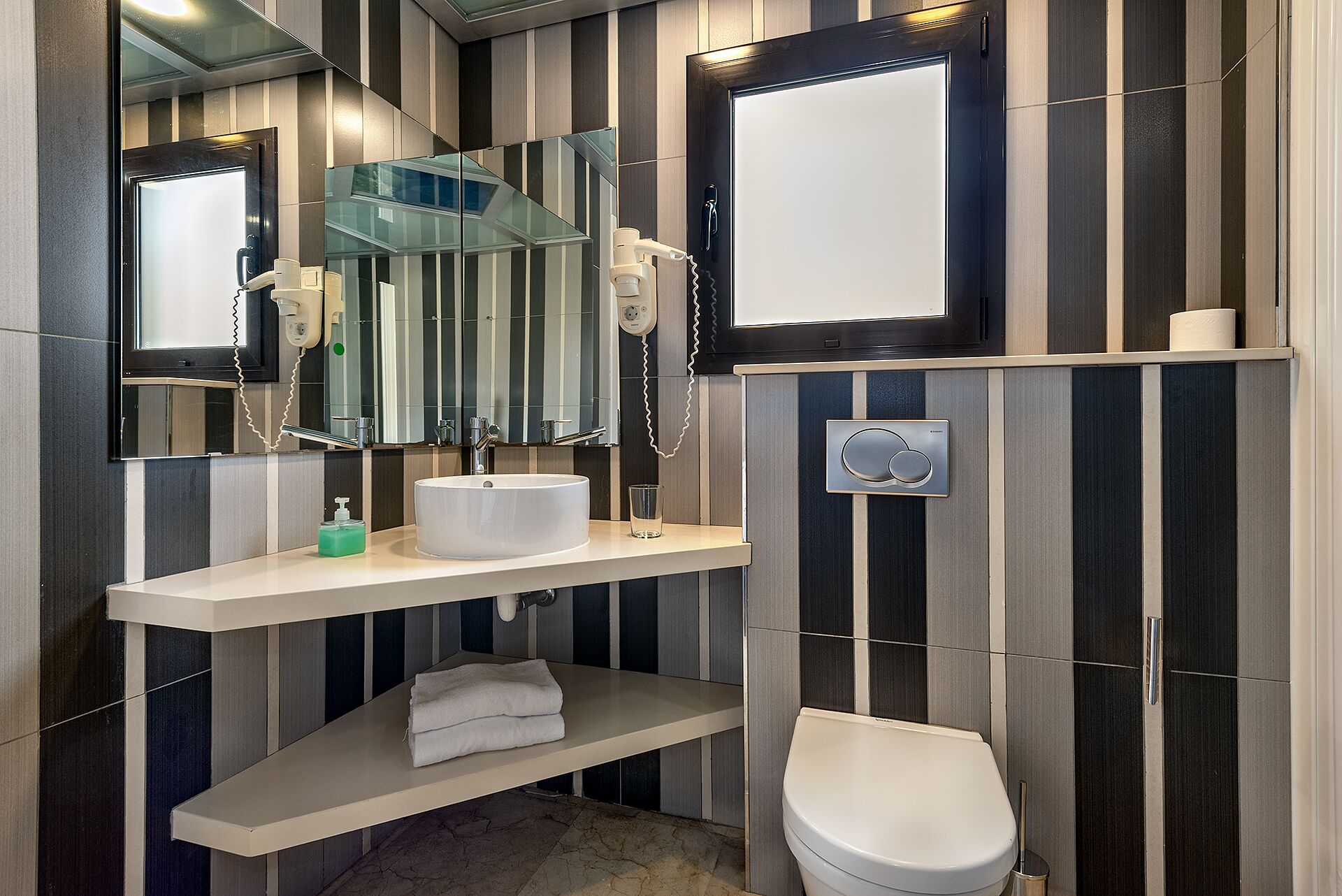 Un bagno moderno con uno specchio grande, un lavandino, un water e un portasciugamani.