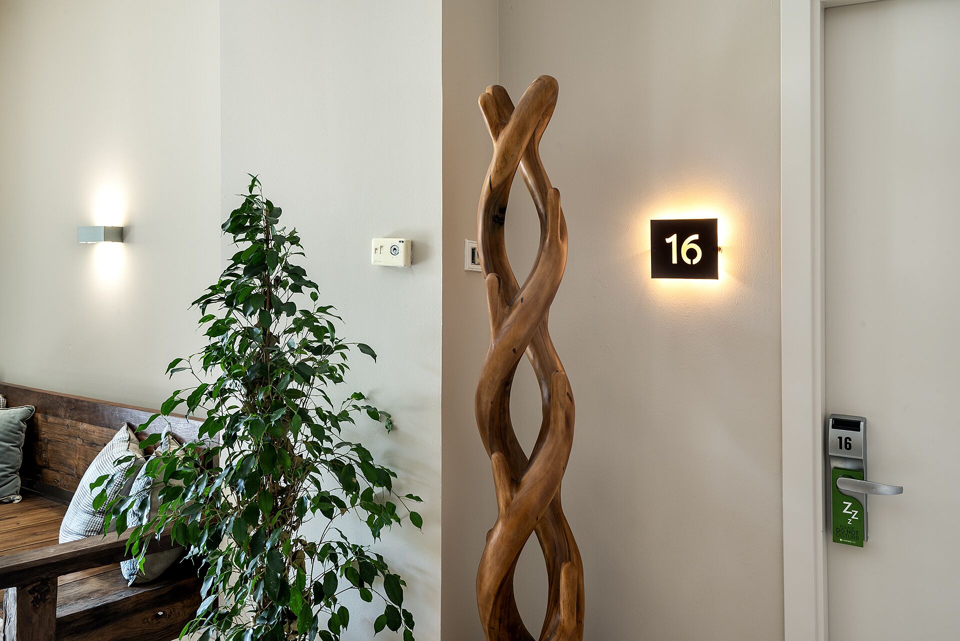 Un interior moderno con una escultura de madera, una planta y un cartel con el número 16.
