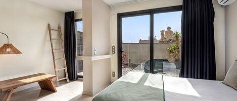 A hotel room with a bed, a bench, a ladder, and a view of the cityscape through large windows.