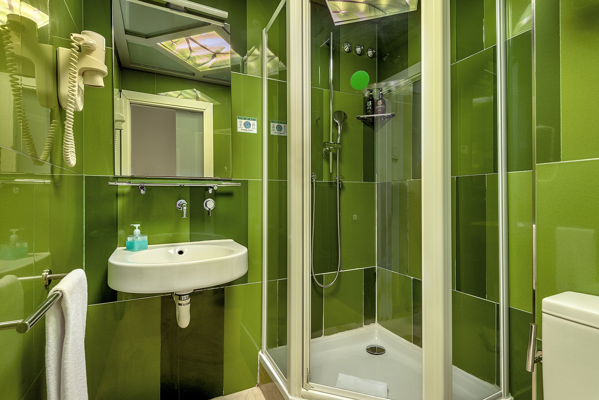 A bathroom with green tiles, a white sink, a glass-enclosed shower, and a telephone.