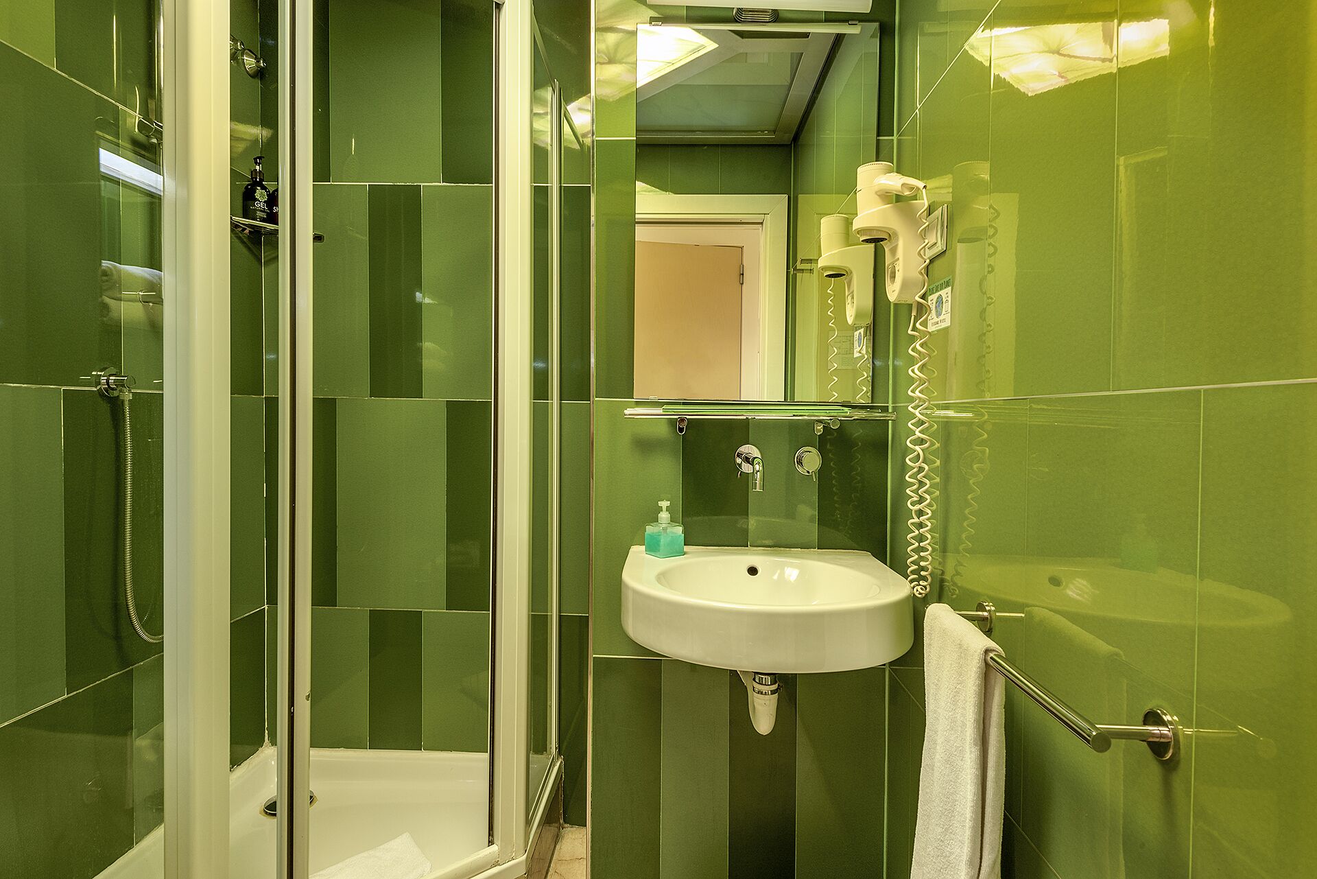 A bathroom with green tiles, a white sink, a glass shower enclosure, and a towel rack.