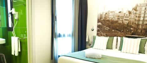 A hotel room with a bed, a bathroom with a green wall, and a cityscape view.