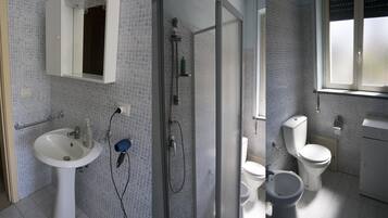 A bathroom with a sink, a glass-enclosed shower, two toilets, and a window.