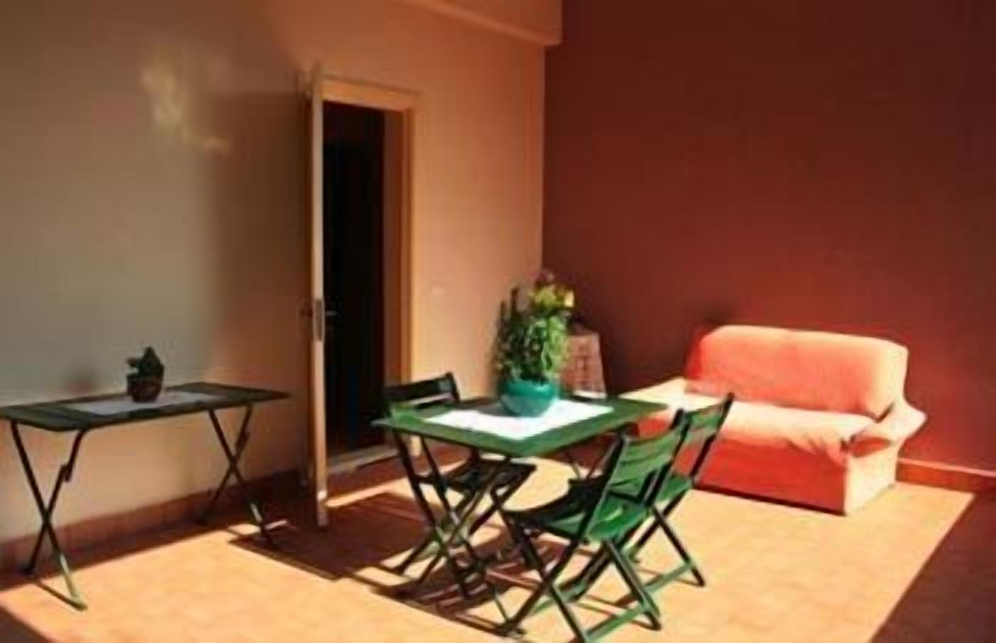 Una habitación pequeña e iluminada por el sol, con una mesa y sillas verdes, un sofá rojo y una planta en maceta.