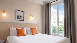Habitación de hotel con una cama grande, dos lámparas de pared, un cuadro enmarcado y una ventana con cortinas.