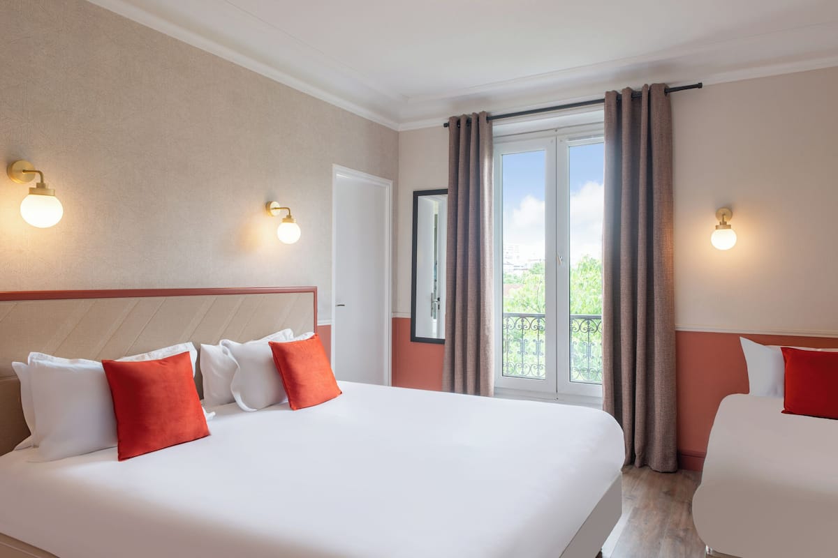 Une chambre d’hôtel avec un grand lit, deux tables de chevet, une fenêtre avec des rideaux et des lampes fixées au mur.