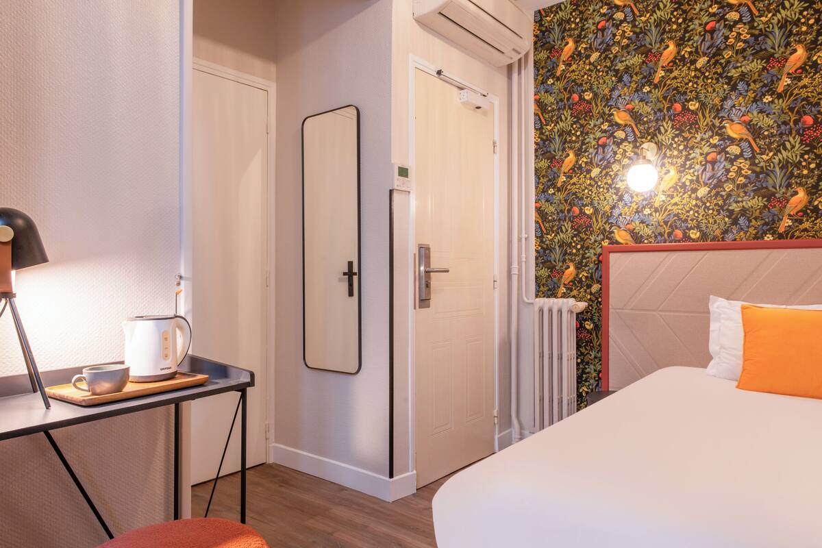 Une chambre d’hôtel avec un lit, un bureau doté d’une bouilloire, un miroir, un radiateur et une porte.