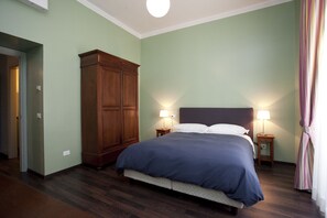A bedroom with a large bed, two bedside lamps, a wardrobe, and a door leading to another room. - Santi Quattro al Colosseo (Rome)
