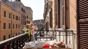 A balcony with a tray of breakfast items, a vase with flowers, and a view of historic buildings. - Santi Quattro al Colosseo (Rome)