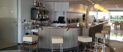 Zona de bar moderna con una barra curva, taburetes y una máquina de café.