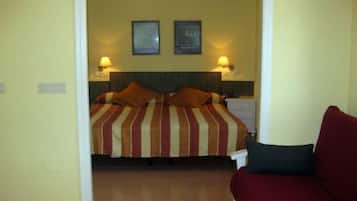 Una habitación de hotel con una cama, dos lámparas de noche, una mesita de noche y un sofá rojo.