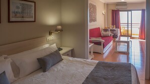 Habitación de hotel con cama, mesita de noche, lámpara y vistas al balcón, que tiene una mesa y sillas.