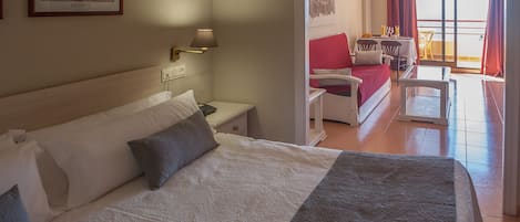 A hotel room with a bed, bedside table, lamp, and a view of the balcony with a table and chairs.