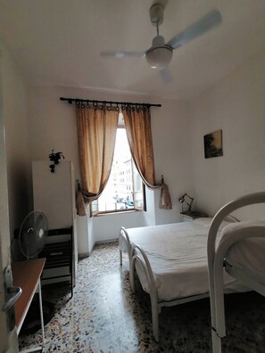 A bedroom with a bed, a ceiling fan, a window with curtains, a radiator, and a wall-mounted lamp. - Prince Inn (Rome)