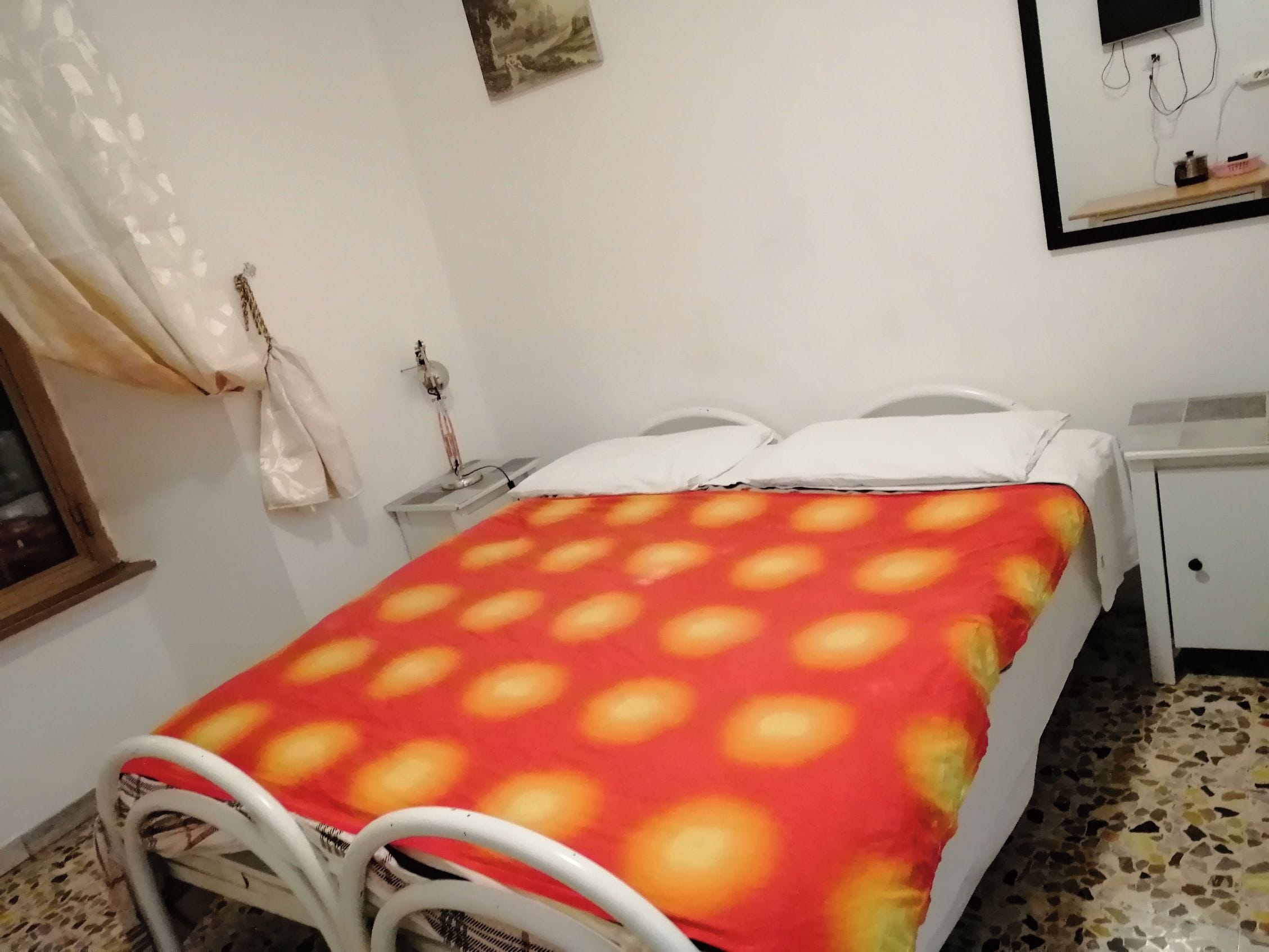 Una cama individual con una colcha estampada, una mesita de noche y un espejo en la pared.