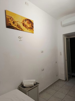 Quarto de hotel com cama, mesa de cabeceira pequena com toalha, ar condicionado e um quadro na parede.