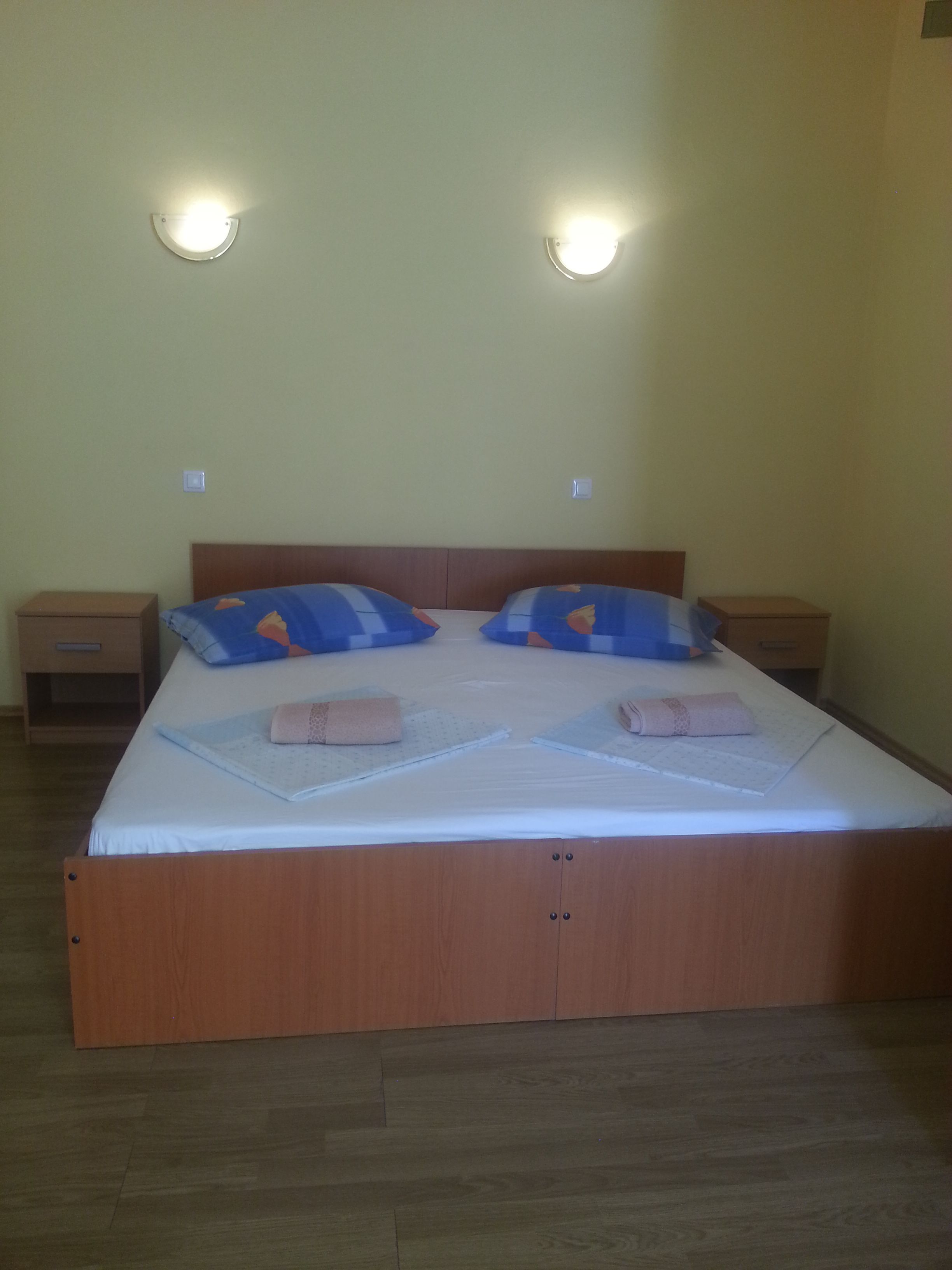 A single bed with a wooden frame, two nightstands, and two wall-mounted lights.