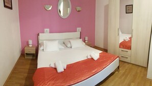 A neatly made bed with white linens and a red blanket, a bedside table with a lamp, and a mirror on the wall. - Villa Angela (Split)