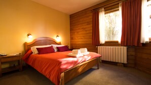 Un lit en bois avec un couvre-lit rouge et des oreillers, une table de chevet avec une lampe, et une fenêtre avec des rideaux.