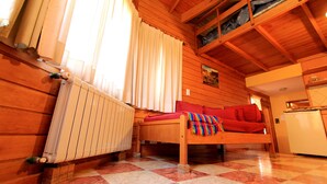 Une cabane en bois chaleureuse, avec un lit, un radiateur, une fenêtre avec des rideaux et un coin cuisine.