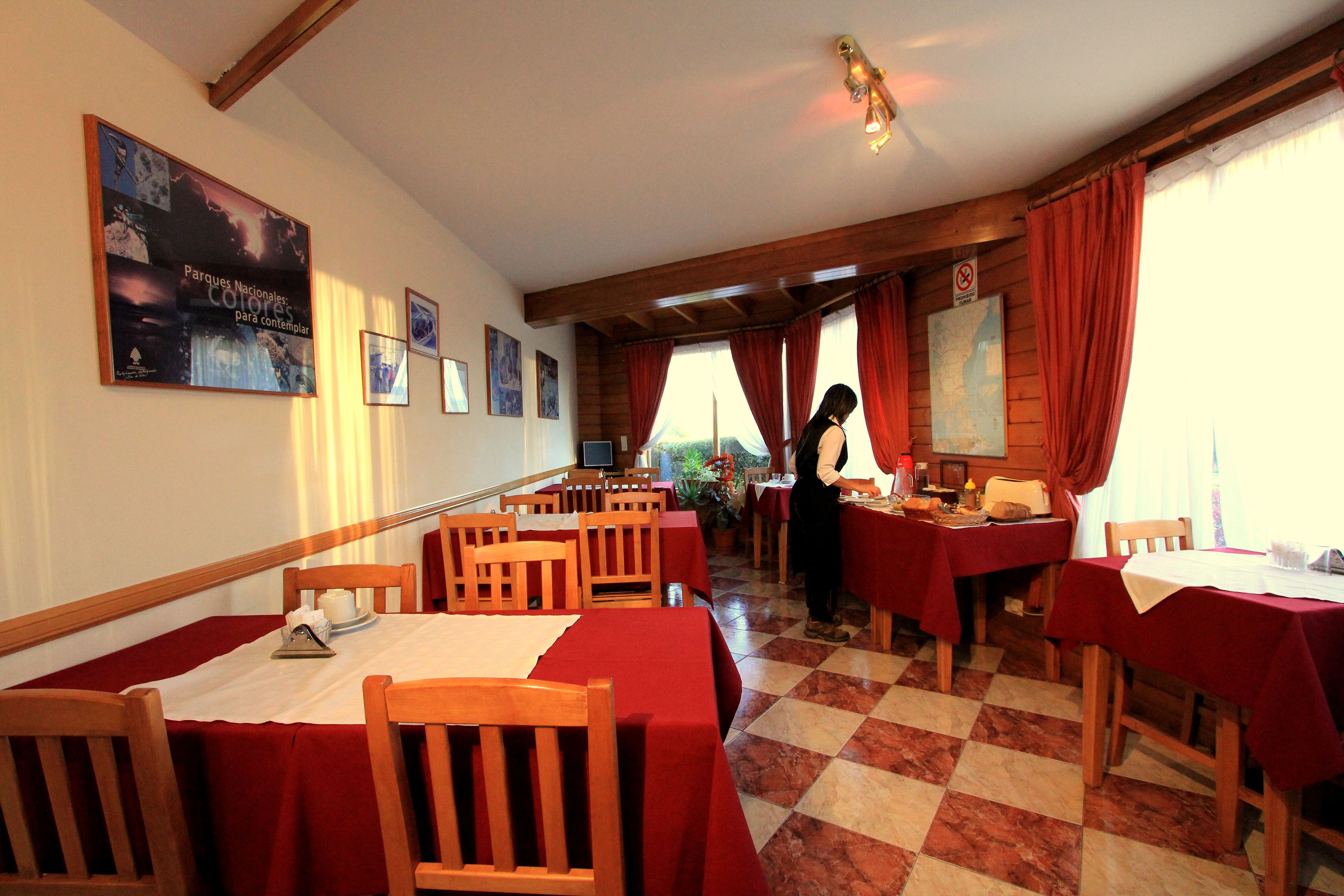 A restaurant with wooden tables and chairs, red tablecloths, and a waitress.