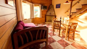 Une pièce chaleureuse avec des murs en bois, un sol à carreaux, une cheminée, une table à manger avec des chaises et un banc.