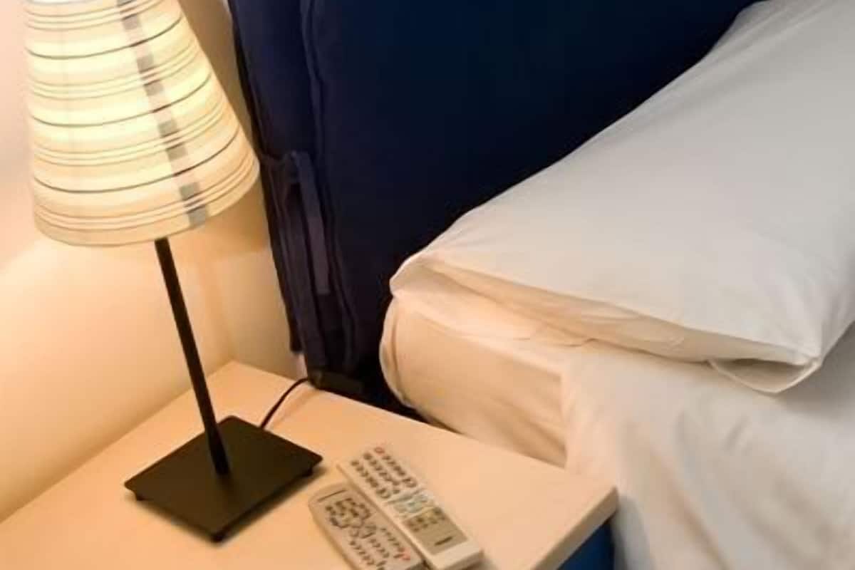 A hotel room with a bedside table, a lamp, a remote control, a blue drawer, and a patterned floor.