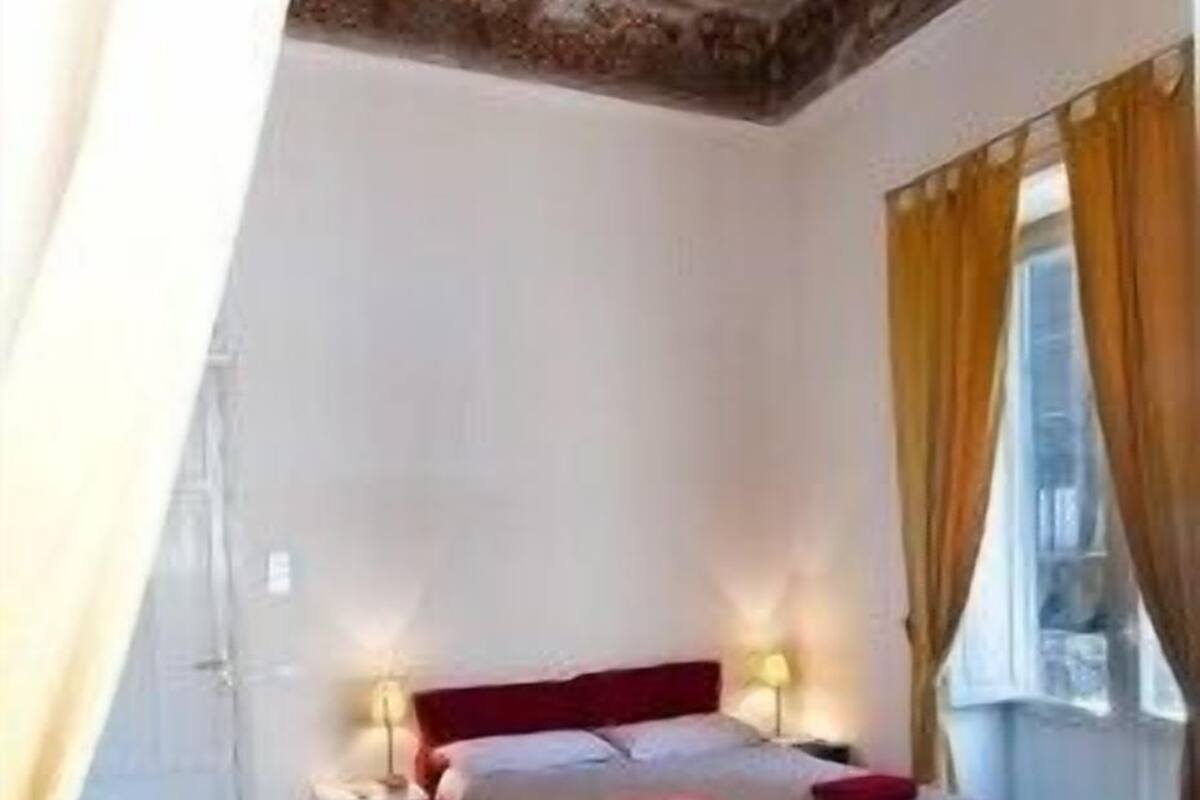 A bedroom with a bed, bedside tables, a window with curtains, and a chair.