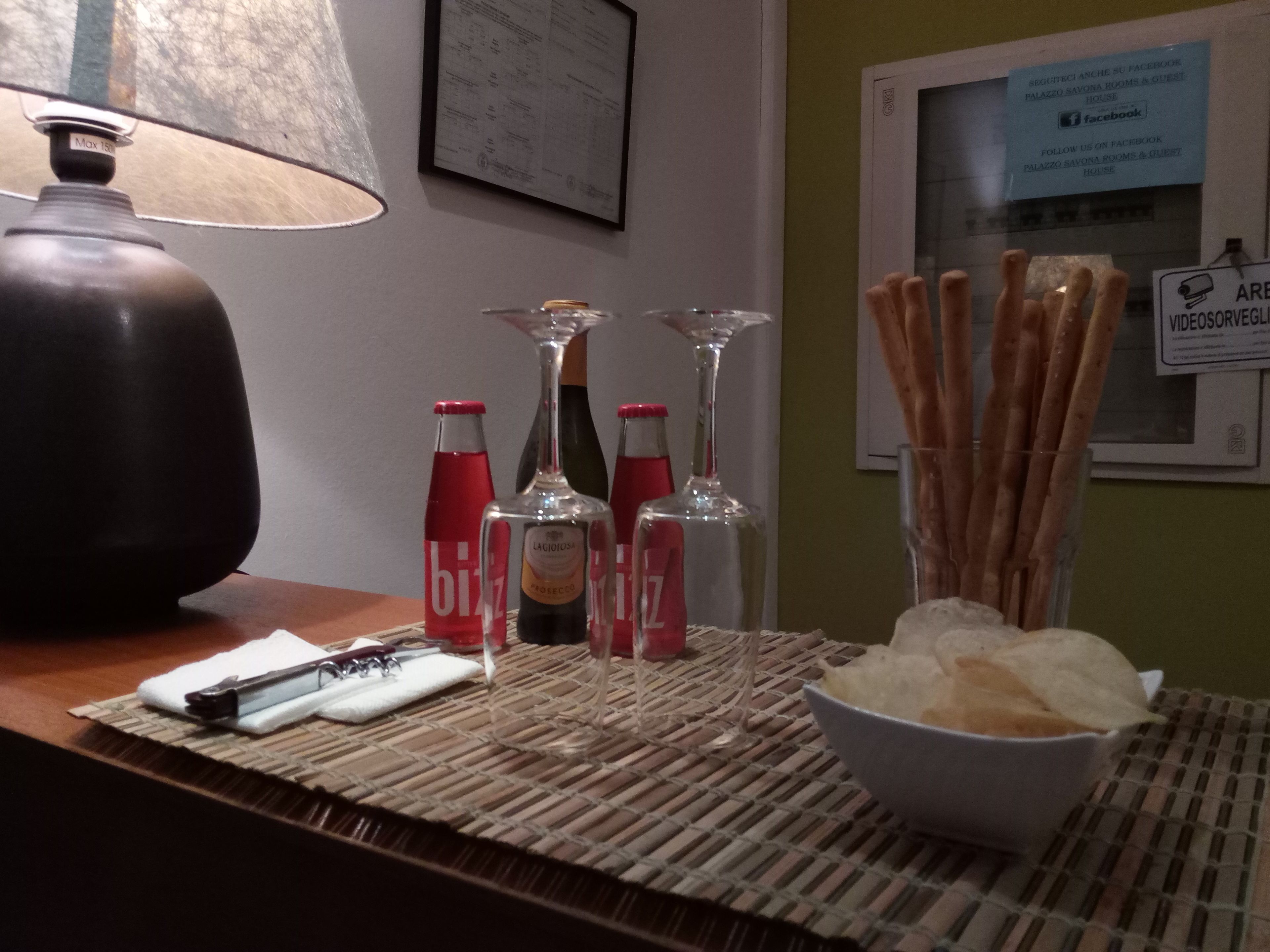 Un tavolo con una lampada, bottiglie, bicchieri e qualche snack.