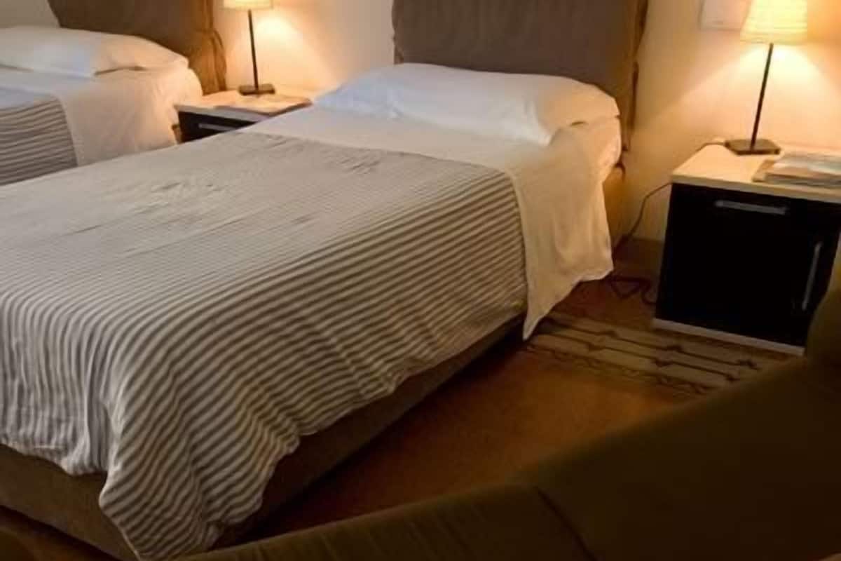 A hotel room with two beds, each with a headboard and bedside tables with lamps.
