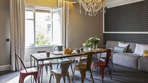 A dining area with a table set for four, surrounded by chairs, a chandelier, and a view of greenery outside. - Ainb B&B Eixample Muntaner (Barcelona)