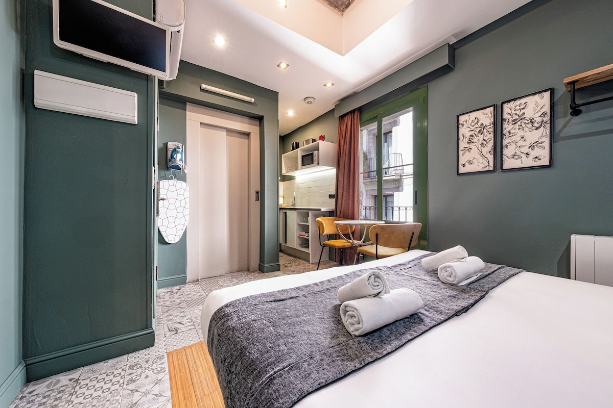 Habitación de hotel con cama, escritorio y silla. Hay una ventana con cortinas, un televisor montado en la pared y obras de arte.