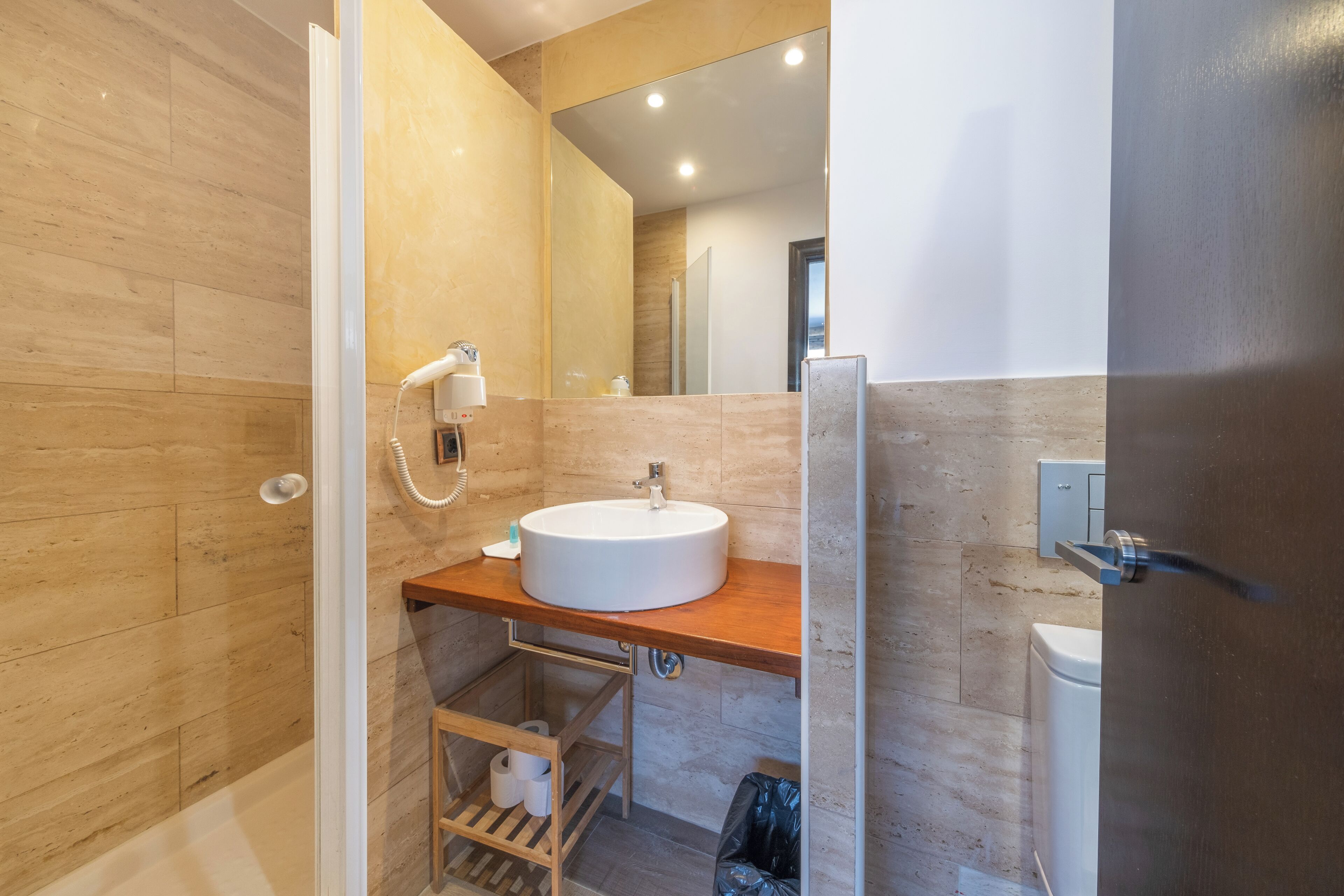 A modern bathroom with a wooden vanity, a white sink, and a glass shower enclosure.