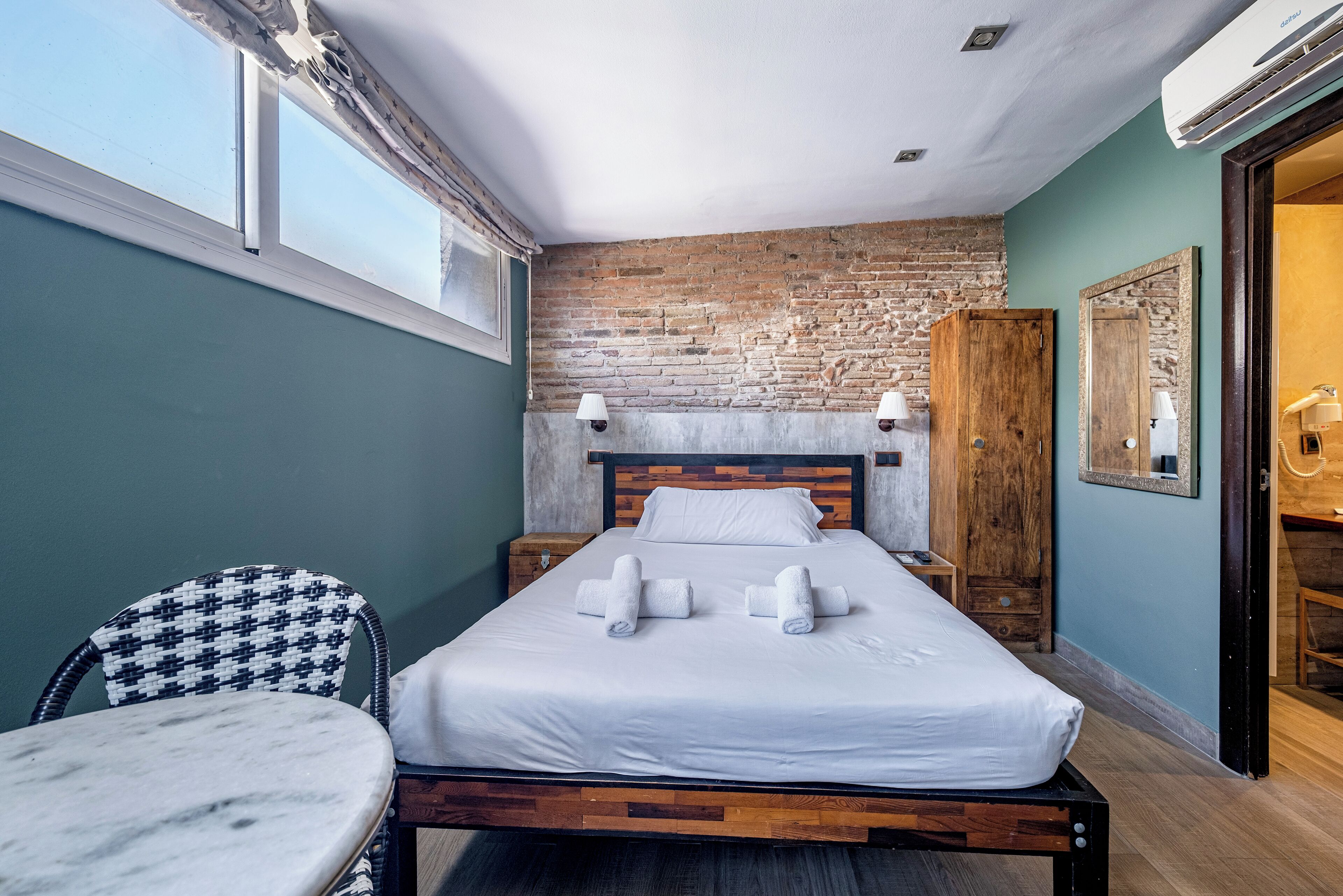 A neatly made bed with white linens and towels, a wooden headboard, and a brick wall.