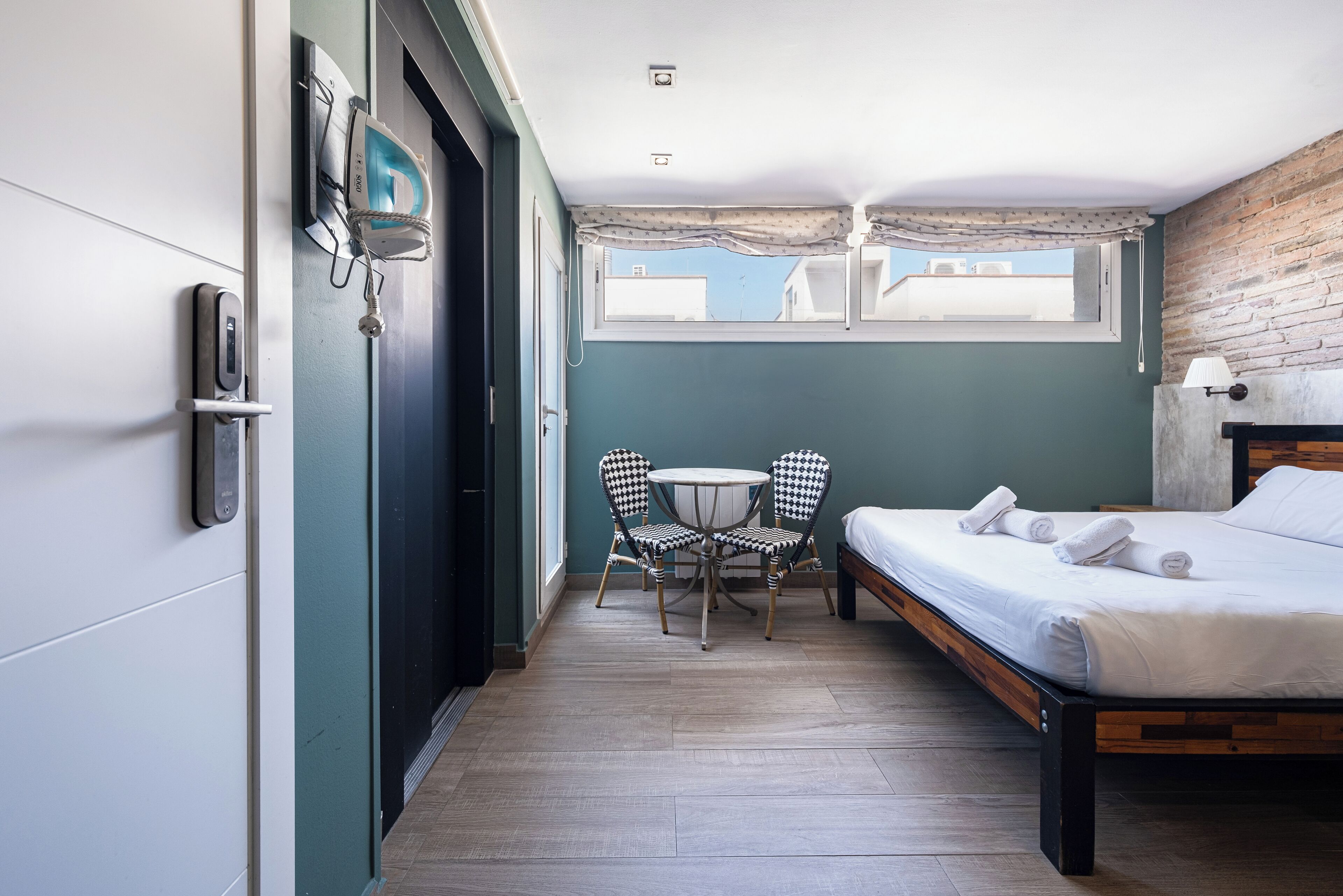 A room with a bed, a small table with chairs, a window, and a door.