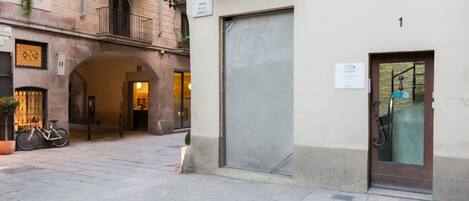 A narrow street with a closed shop door, a bicycle, and a manhole cover.