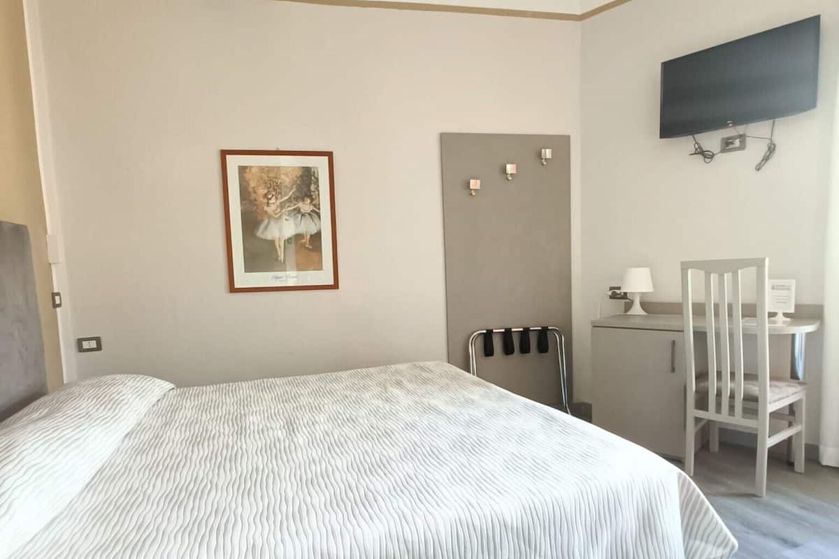 Un dormitorio con cama, escritorio, silla, televisor y un cuadro en la pared.