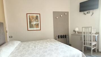 A bedroom with a bed, a desk, a chair, a television, and a framed picture on the wall.
