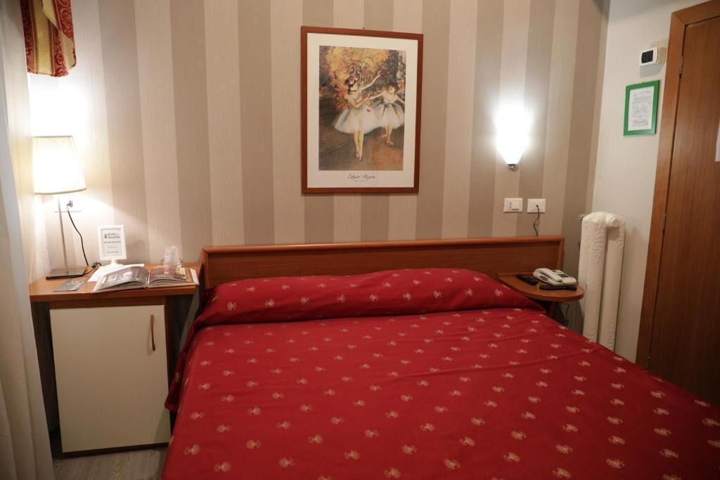 A hotel room with a bed, a desk with a lamp, a telephone, and a small cabinet.