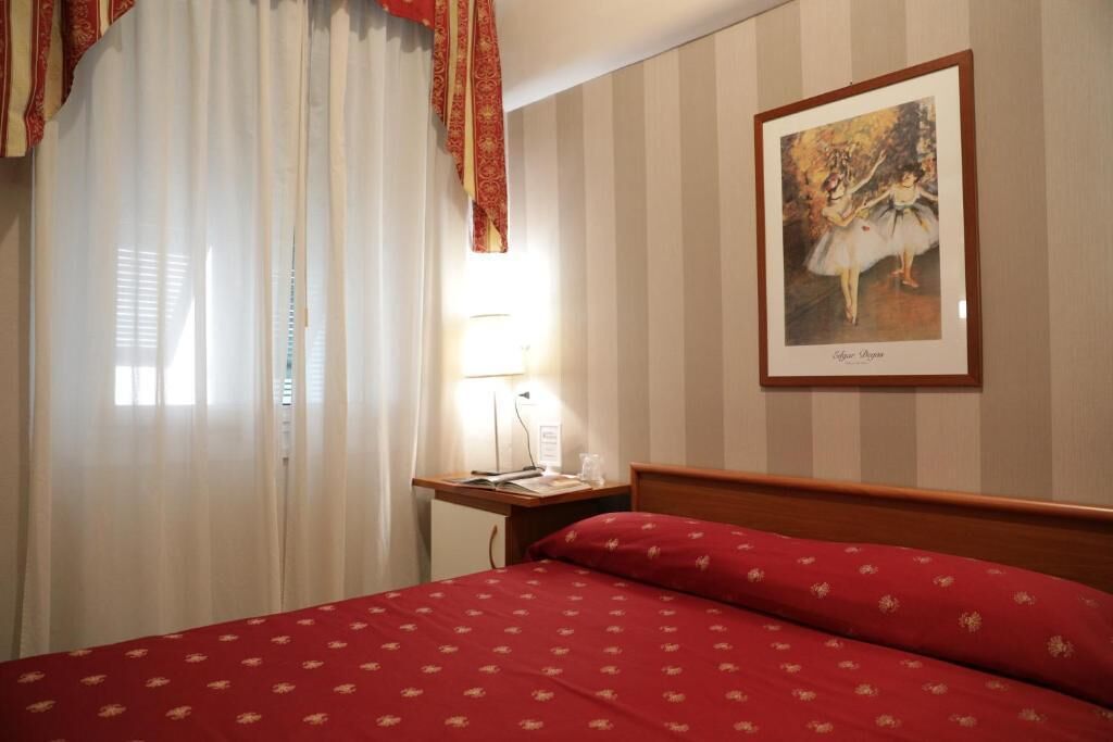 A hotel room with a bed, a desk, a lamp, and a framed picture on the wall.