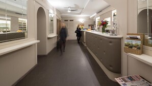 A hotel corridor with a reception desk, a mirror, and a counter with a vase of flowers. - Hotel Helvetia (Genoa)