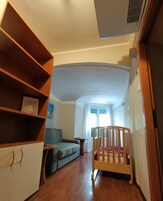 Une pièce avec une armoire en bois, un canapé gris, un berceau en bois et une fenêtre avec des rideaux.
