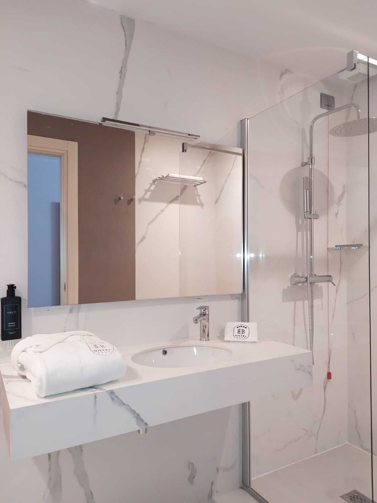 Un baño moderno con lavamanos de mármol, un espejo, una toalla y una ducha con cerramiento de vidrio.