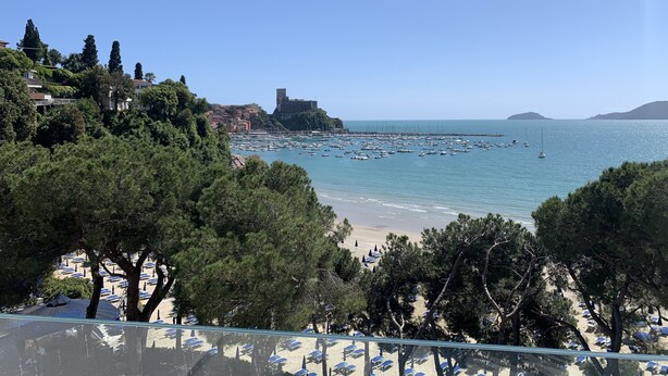 Vista costera con playa, barcos y un edificio histórico.