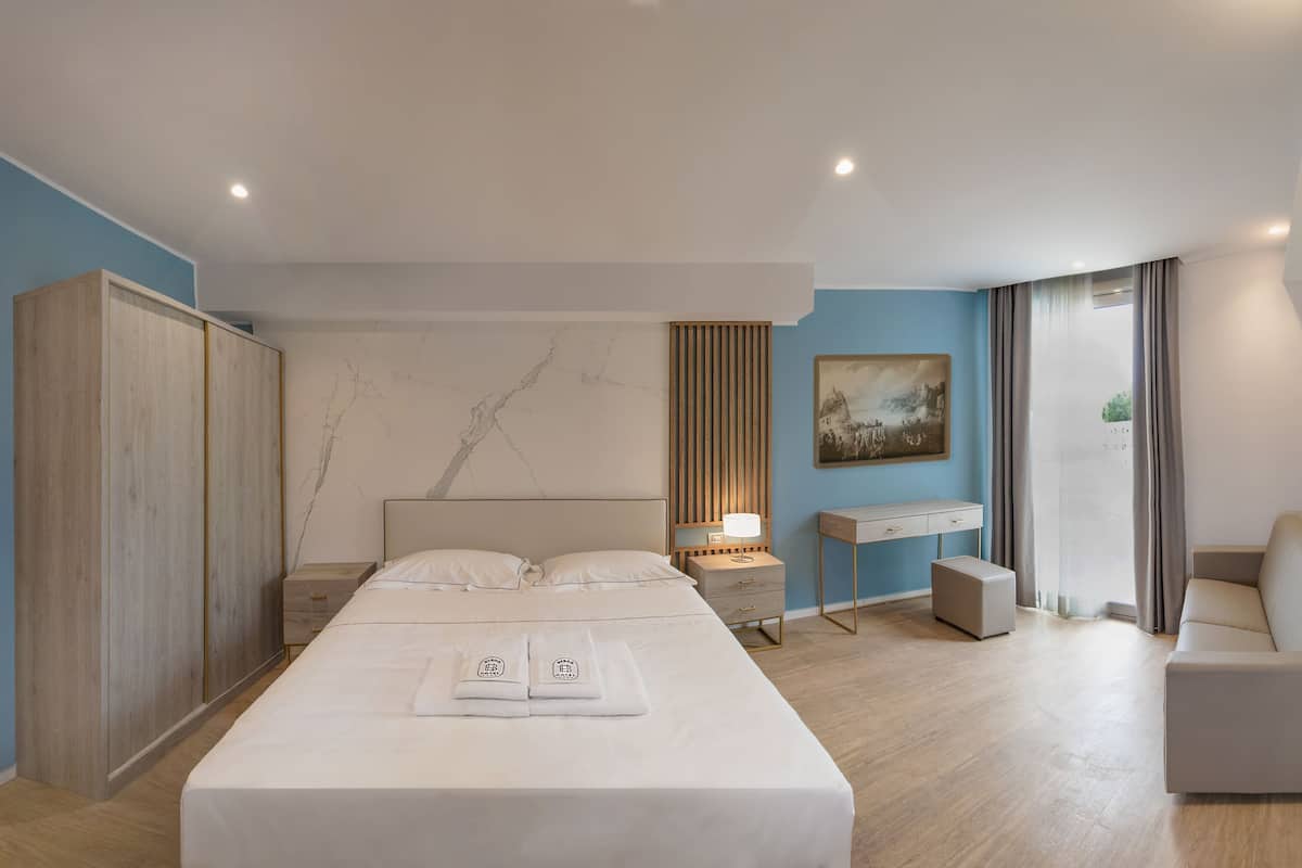 Une chambre d’hôtel moderne équipée d’un grand lit, d’une table de chevet, d’un bureau, d’un canapé et d’une armoire.