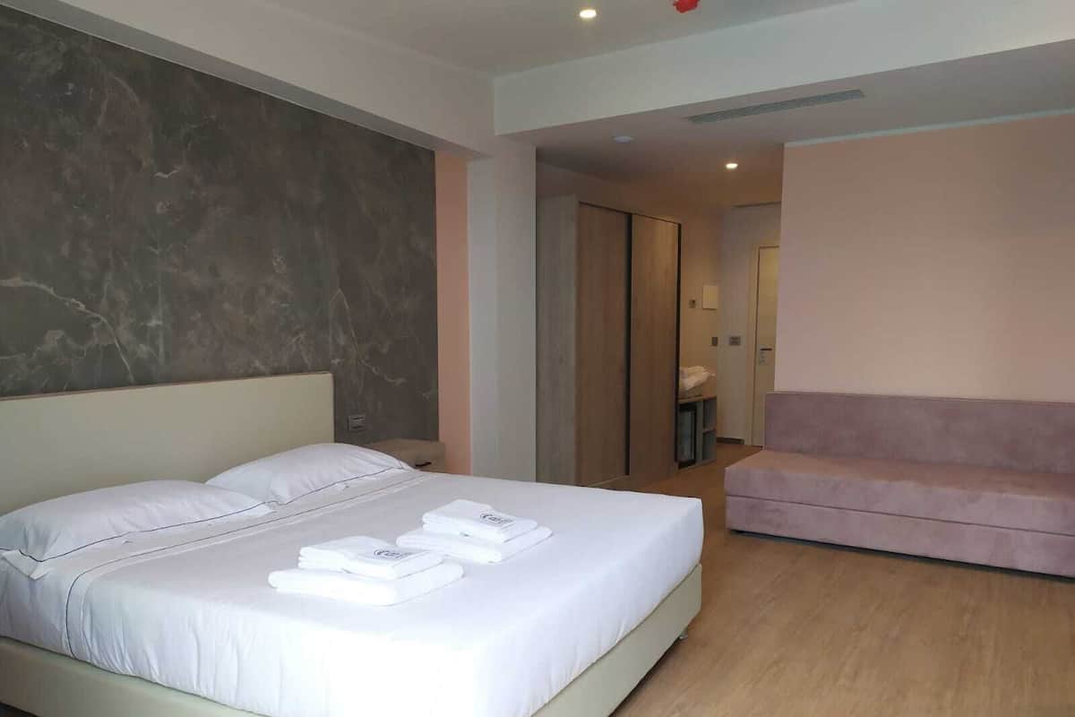 Une chambre d’hôtel moderne avec un grand lit, un canapé rose et un mur décoratif en marbre.